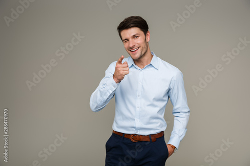 Fotografie Image of cheerful brunette man wearing formal clothes smiling and pointing finge