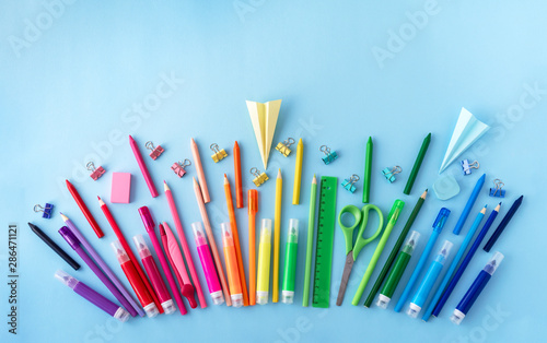 Variety of school supplies in rainbow colors sequence on pastel blue background. Flat lay style. Back to school concept.
