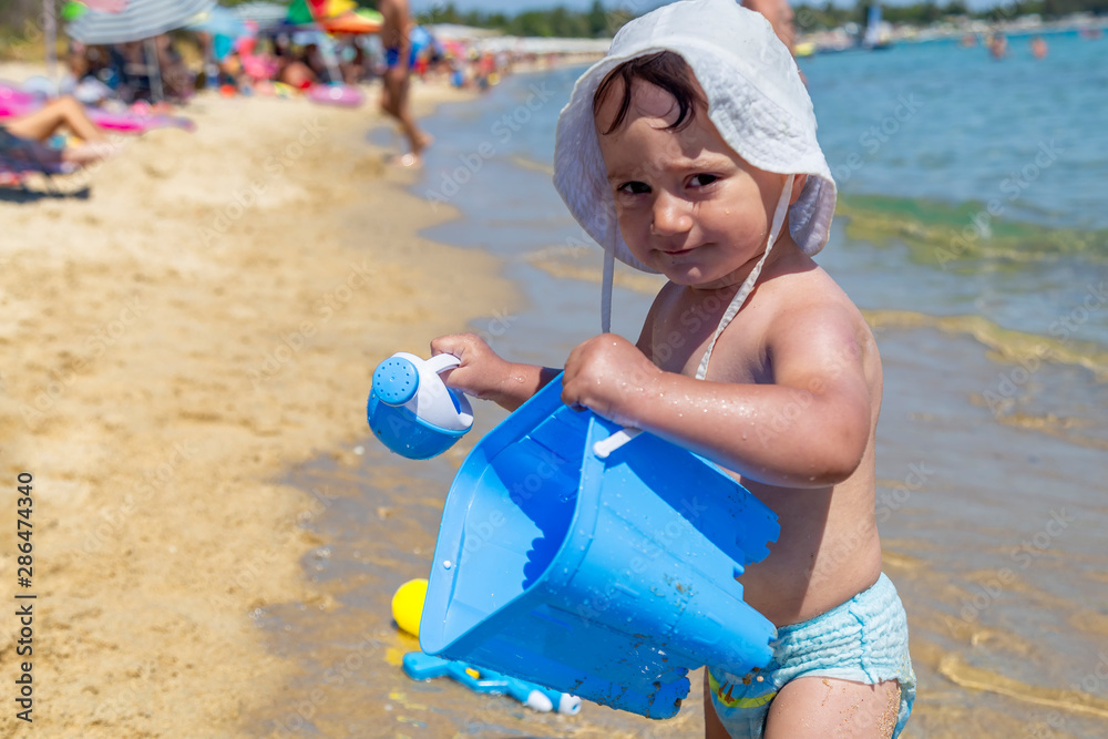 Little kid on the beach with blue bucket and sand toys Little kid on the beach with blue bucket and sand toys