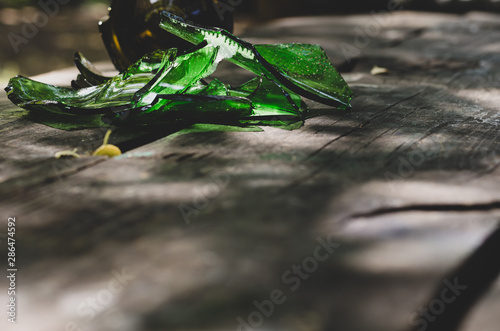 Two broken green and brown glass wine bottles on a wooden table in the background. Foreground is free. Without anyone. Close-up. Shooting at the table level. Soft focus. Horizontally photo