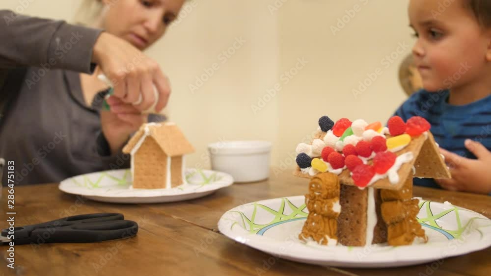 Mother and boy decorating his fun gingerbread house in the kitchen