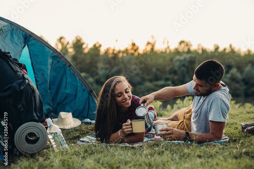 happy young couple drinking coffee, camping together by the river