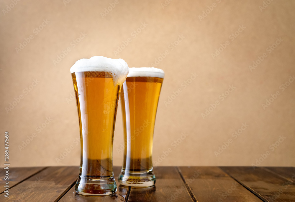 Two light beer glasses w on the light yellow background - obrazy, fototapety, plakaty 