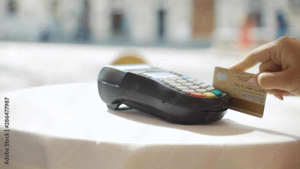 Close up hands woman paying in the cafe by credit card swiping with credit card on pos payment terminal on table in sunlight customer machine money terminal cash client electronic slow motion