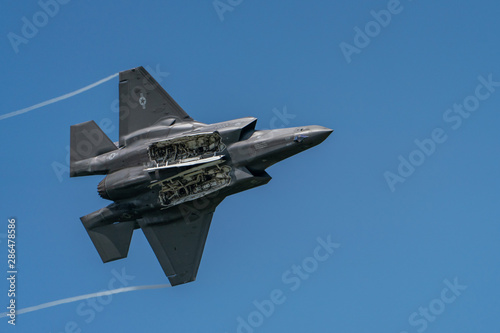 F35 Lightning II Jet Fighter in banking climb with bomb doors open against blue sky