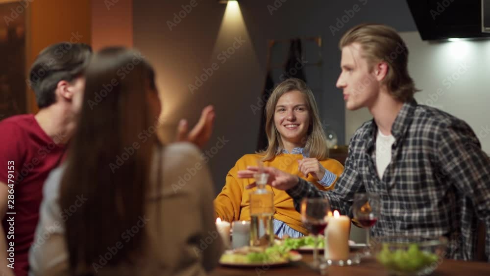 Group of four young friends, two couples, sitting at table in domestic kitchen and enjoying talking over dinner and wine. Selective focus on blonde woman listening to boyfriend Group of four young friends, two couples, sitting at table in domestic kitchen and enjoying talking over dinner and wine. Selective focus on blonde woman listening to boyfriend