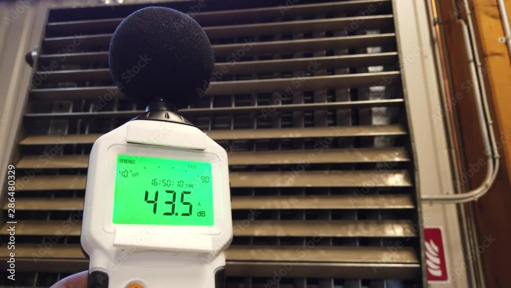Sound level meter measuring the noise of industrial ventilation unit.