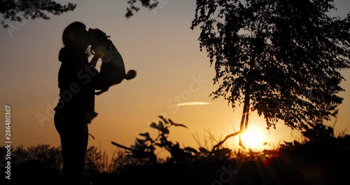 A woman kisses her dog on a sunset background. Silhouette of a woman and a dog. Pet love