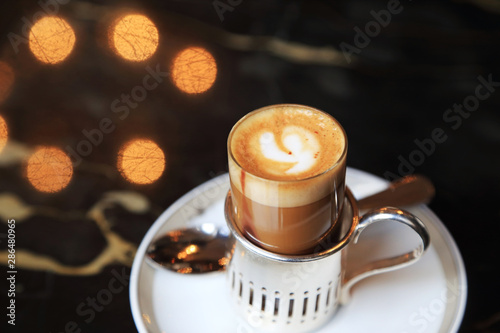 Small shot of espresso with steamed hot milk and cream on cafe table with light bokeh on background.