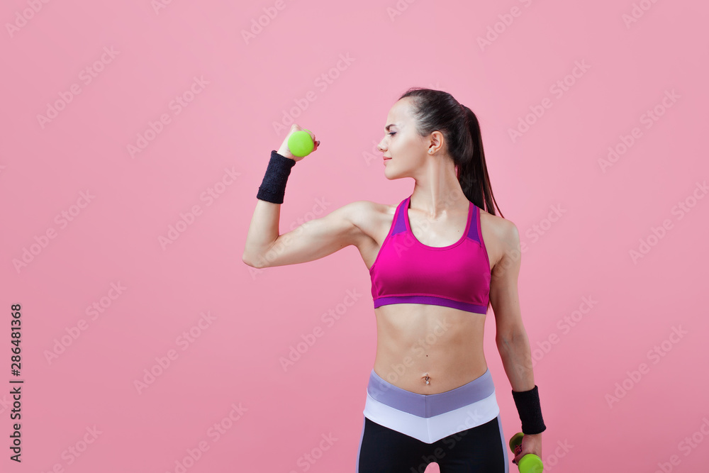 A young athletic attractive brunette girl with a ponytail shows off her biceps, holding dumbell in hand. Girl power. A young athletic attractive brunette girl with a ponytail shows off her biceps, holding dumbell in hand. Girl power.