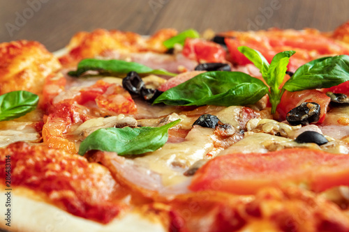 Pizza on a wooden background with ham, olives, tomatoes and green basil. Itolyan cuisine, copy space.