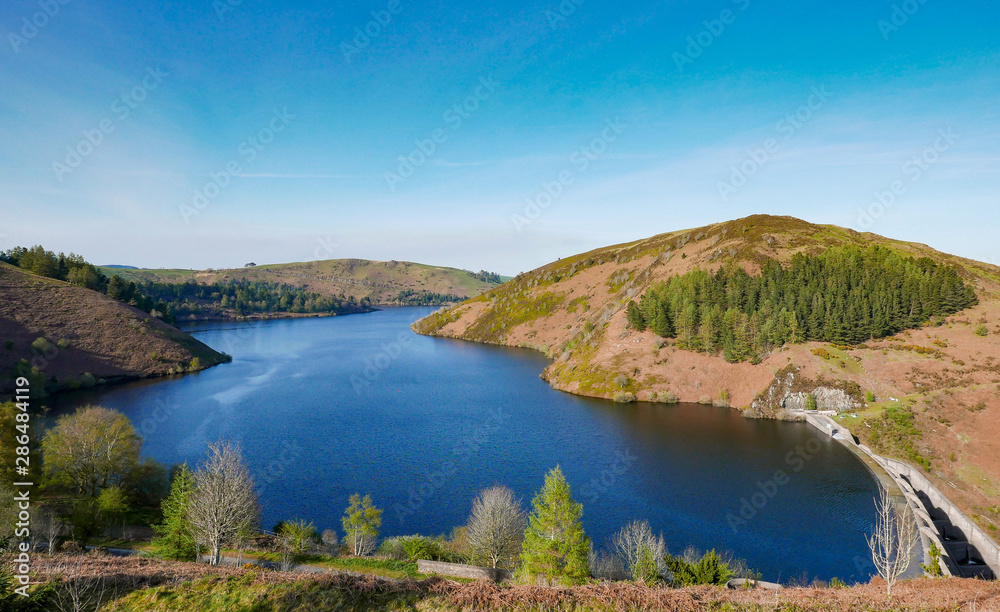 Llyn Clywedog reservoir in Wales with blue skies and trees.