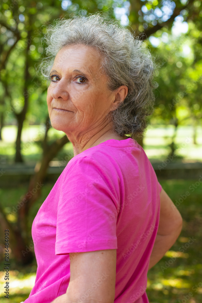 Serious confident old lady walking in park. Side and back of senior grey haired woman in casual turning face to camera. Senior woman outdoors concept Serious confident old lady walking in park. Side and back of senior grey haired woman in casual turning face to camera. Senior woman outdoors concept