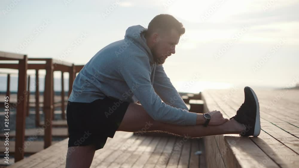 Man doing leg stretch exercise outdoor at sunset Man doing leg stretch exercise outdoor at sunset