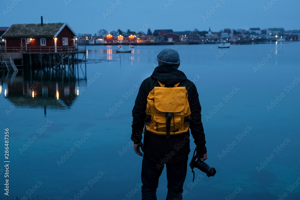 Traveler man with a yellow backpack standing on the background of night Lofoten Reine