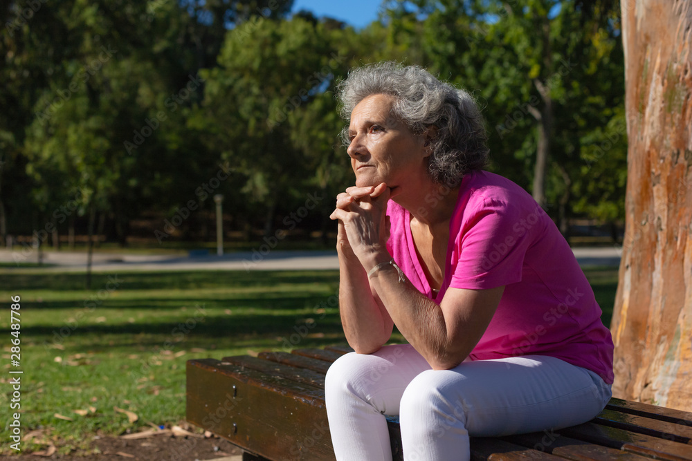 Pensive lonely old lady spending leisure time in park. Senior grey haired woman in casual sitting on bench outdoors, leaning chin on hands and thinking. Old lady outdoors concept