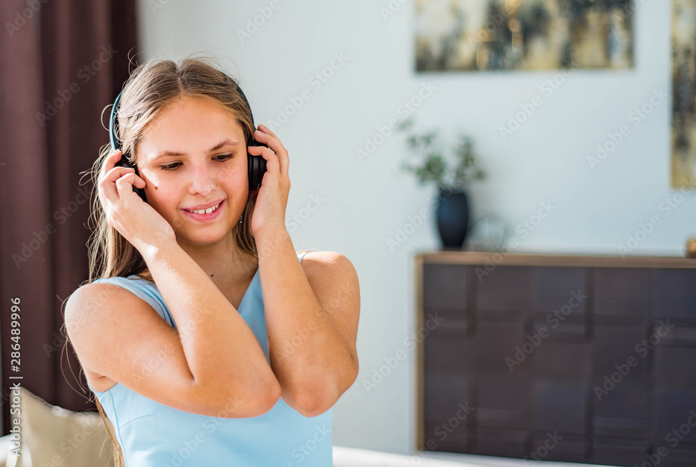 portrait of young teenager brunette girl with long hair in blue dress listening music on headphones in room portrait of young teenager brunette girl with long hair in blue dress listening music on headphones in room