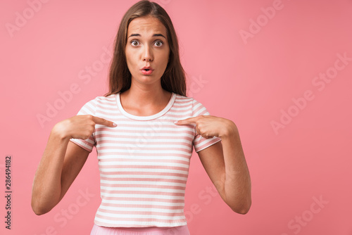 Image of confused young woman wearing striped clothes expressing wonder and pointing finger at herself