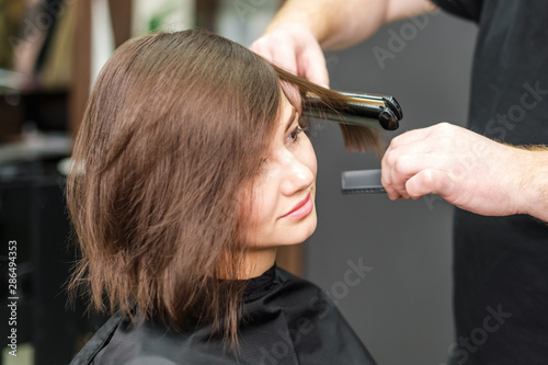 Hairdresser straightening brown hair with hair irons.