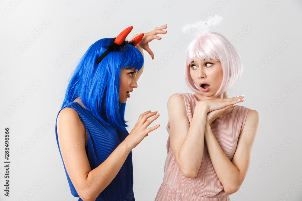 Portrait of angry woman wearing toy devil horns scaring kind girl with halo Portrait of angry woman wearing toy devil horns scaring kind girl with halo