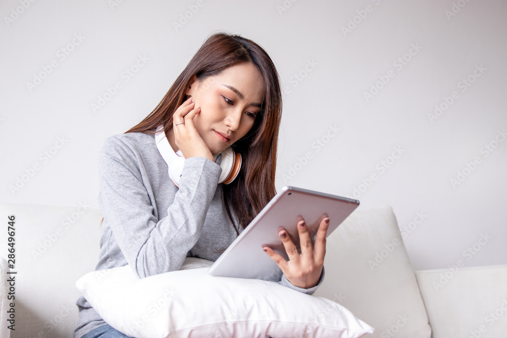 Beautiful Asian woman is using a tablet to shopping online and liaise with customers in the living room. She is the owner of a business selling secondhand goods product online. SME and Business family Beautiful Asian woman is using a tablet to shopping online and liaise with customers in the living room. She is the owner of a business selling secondhand goods product online. SME and Business family