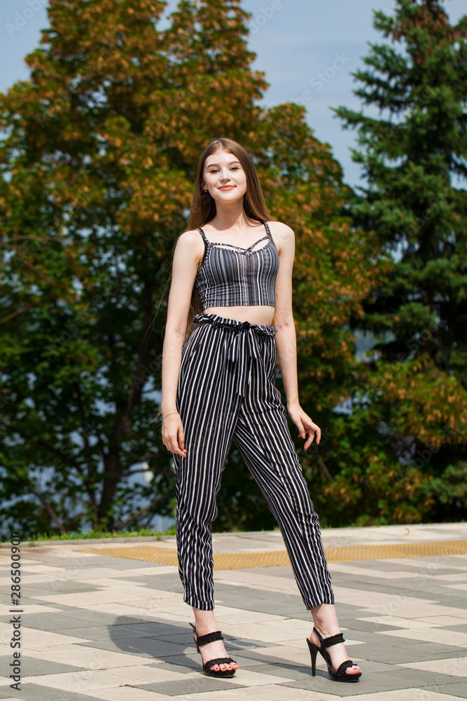 Young beautiful woman in striped trousers walking on the street, summer embankment outdoorst