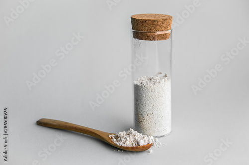 Diatomaceous earth also known as diatomite mixed in glass jar and wood spoon on gray background, studio shot.   photo