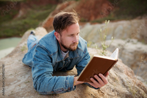 Researcher enthusiastically reading a book lying on the shore of a natural blue lake