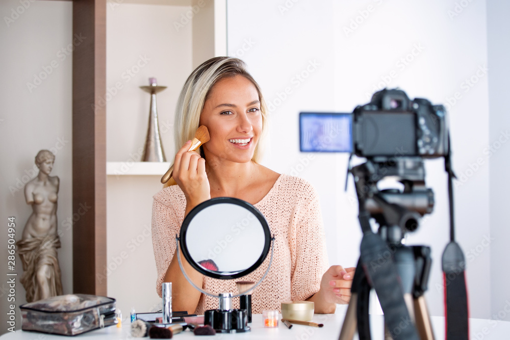 Young beautiful blonde woman professional beauty vlogger or blogger recording make up tutorial to share on social media - obrazy, fototapety, plakaty 