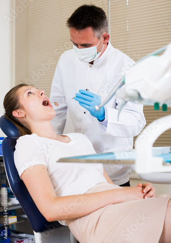 Dentist is treating female visitor which is sitting in dental chair