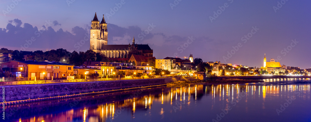 Magdeburg an der Elbe mit Magdeburger Dom, Johanniskirche, mit Promenade am Ufer des Flusses in Abendstimmung mit Abendrot und beleuchteten Gebäuden im Panorama
