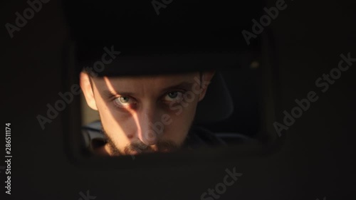 man looks at himself in a mirror while sitting in a car