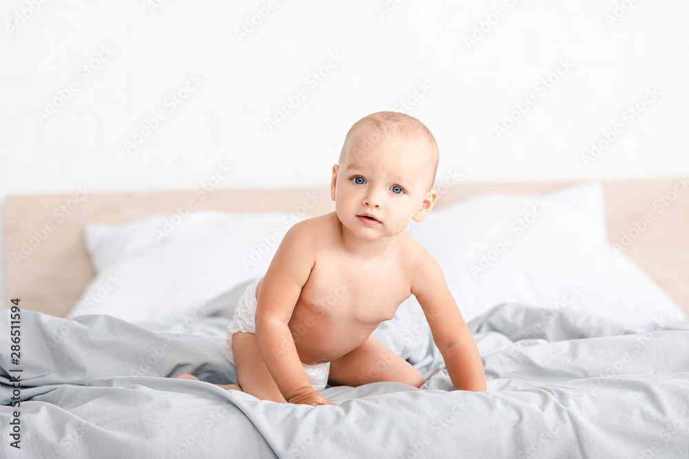 Cute little child sitting on white bed and looking at camera