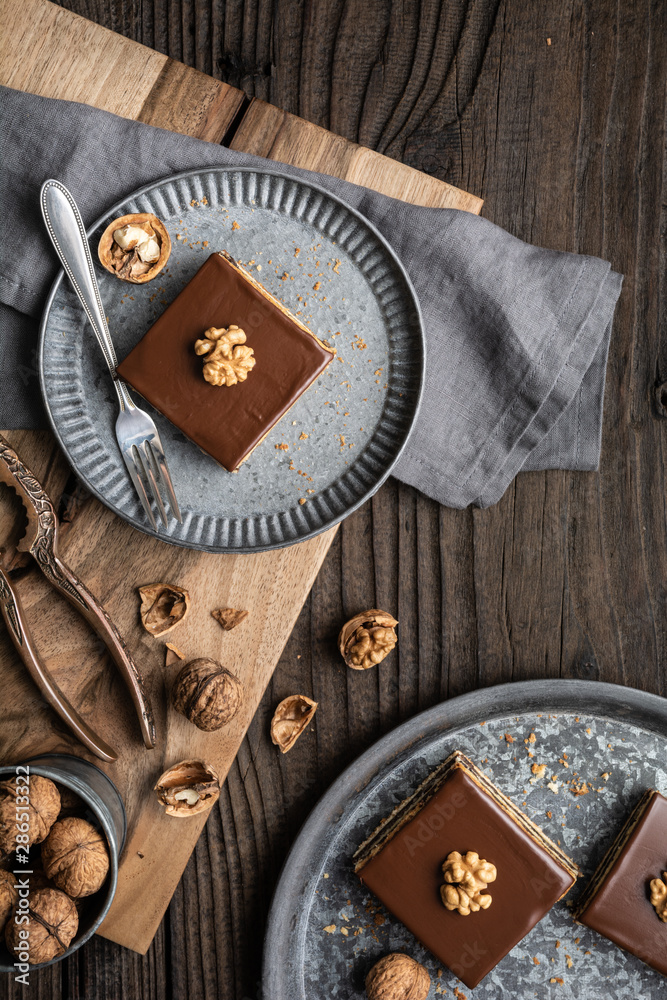 Gerbeaud bars filled with plum marmalade and crushed walnuts, topped with chocolate frosting on wooden background Gerbeaud bars filled with plum marmalade and crushed walnuts, topped with chocolate frosting on wooden background