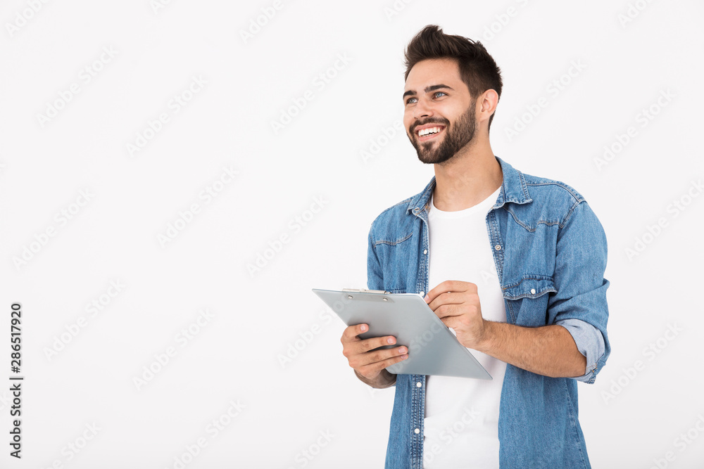 Image of handsome cheerful man holding clipboard and writing while smiling Image of handsome cheerful man holding clipboard and writing while smiling