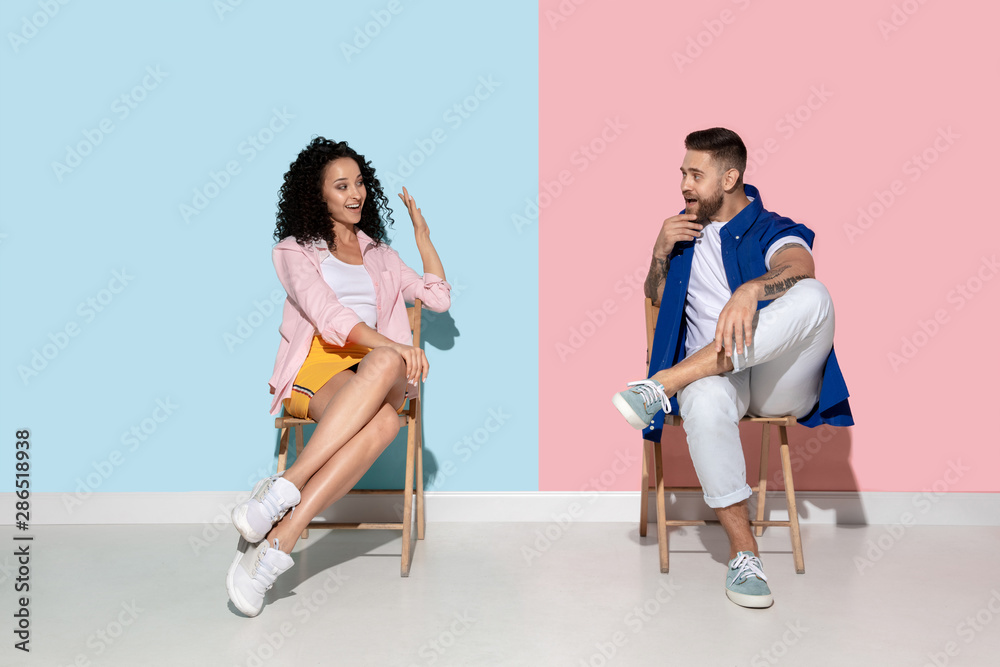 Obraz premium Young emotional man and woman in bright casual clothes posing on pink and blue background. Concept of human emotions, facial expession, ad. Beautiful caucasian couple looks astonished, shocked.