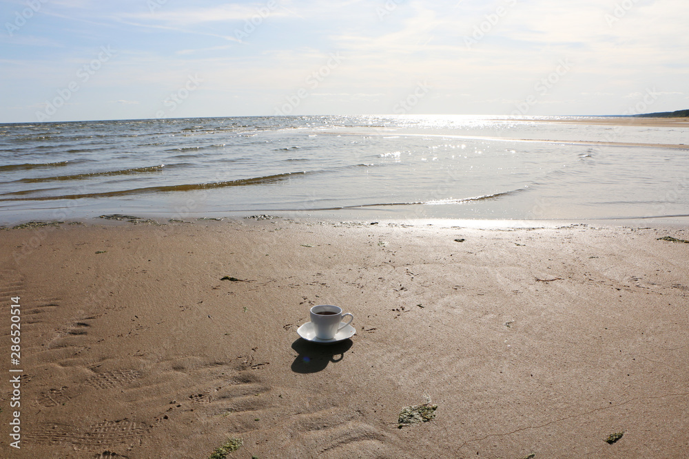 A cup of coffee stands on the sandy seashore