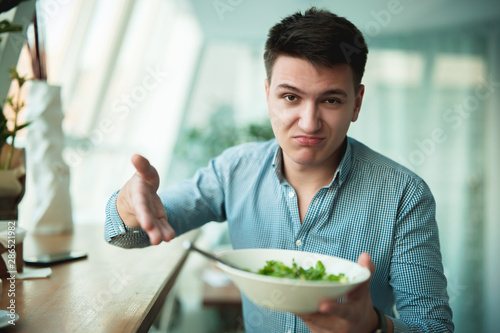 young handsome man is not satisfied with the salad showing it to waiter feeling disappointed