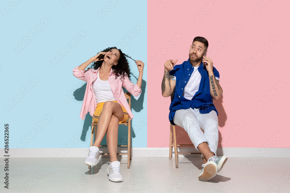 Young emotional caucasian couple in bright casual clothes posing on pink and blue background. Concept of human emotions, facial expession, relations, ad. Woman and man talking on the phone, smartphone