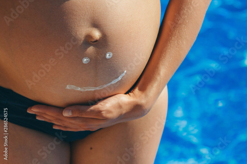 Drawing smile white cream on the belly of a pregnant woman close-up. copy space