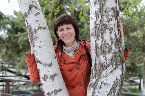 portrait of a lonely older woman with a beautiful face. He looks at the camera and smiles. Walks in the Park, hugs a tree birch and enjoys life. Very happy received the first pension