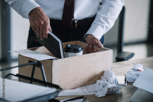 cropped view of man putting notebook in wooden box near paper cup and crumpled paper balls on table