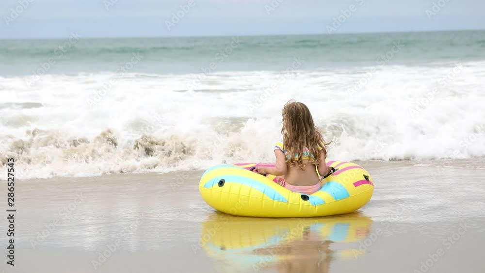 Young girl sitting on float tube at the beach waiting for a wave to roll in so she can ride the water as it pushes her away. Young girl sitting on float tube at the beach waiting for a wave to roll in so she can ride the water as it pushes her away.