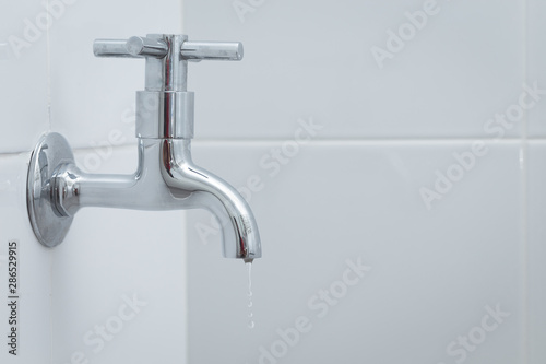 Silver metal faucet on white tile floor