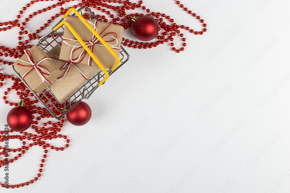 Naklejka premium Gifts in a small shopping basket on a white background with Christmas decorations, concept, copy space.