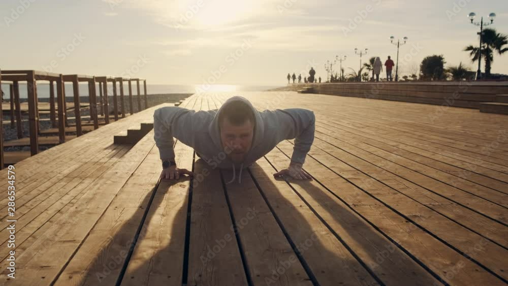 Male athlete is doing push ups on city embankment near sea in sunny evening