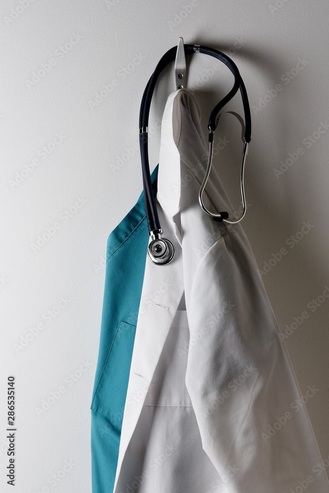 A Doctors White Lab Coat and Green Scrubs Hanging on a Hook with Stethoscope. A Doctors White Lab Coat and Green Scrubs Hanging on a Hook with Stethoscope.