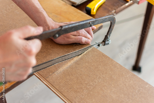 Installation laminate or parquet in the room, worker cuts a laminate of a certain length with a saw