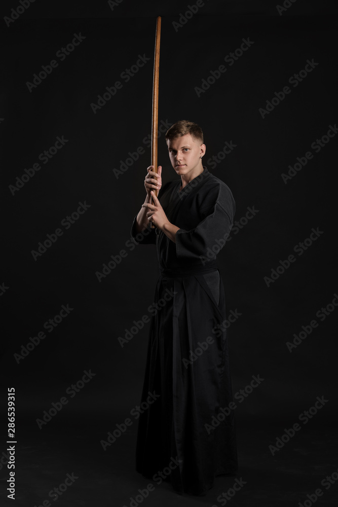 Kendo guru wearing in a traditional japanese kimono is practicing martial art with the shinai bamboo sword against a black studio background. Kendo guru wearing in a traditional japanese kimono is practicing martial art with the shinai bamboo sword against a black studio background.