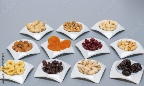 Nuts and dried fruits in white saucers on gray matte background,selective focus and copy space.